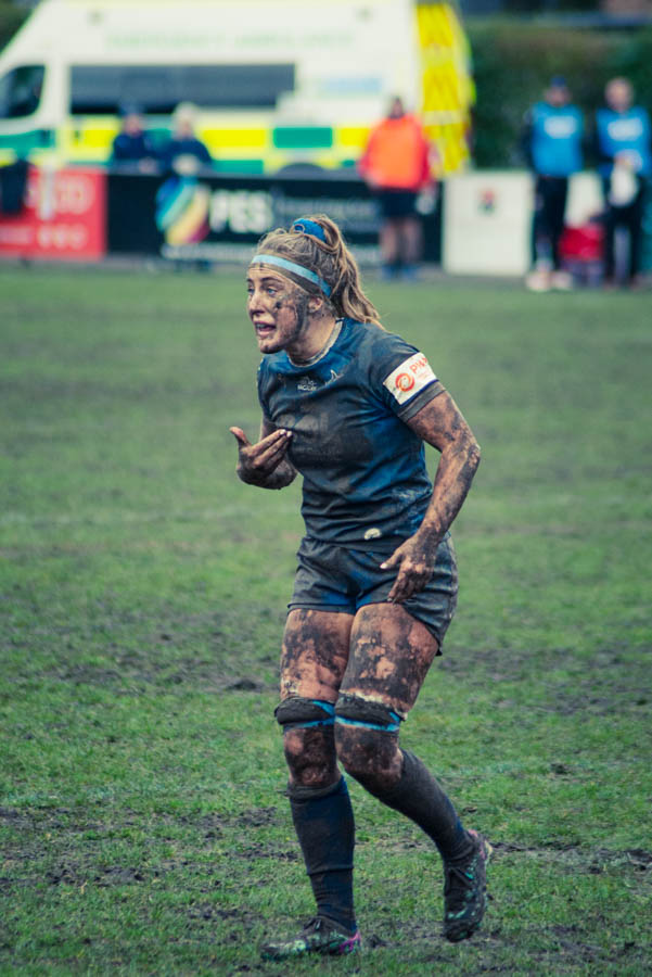 A muddy rugby player in a dark uniform gestures passionately during a match, showcasing determination and intensity on a grassy field.