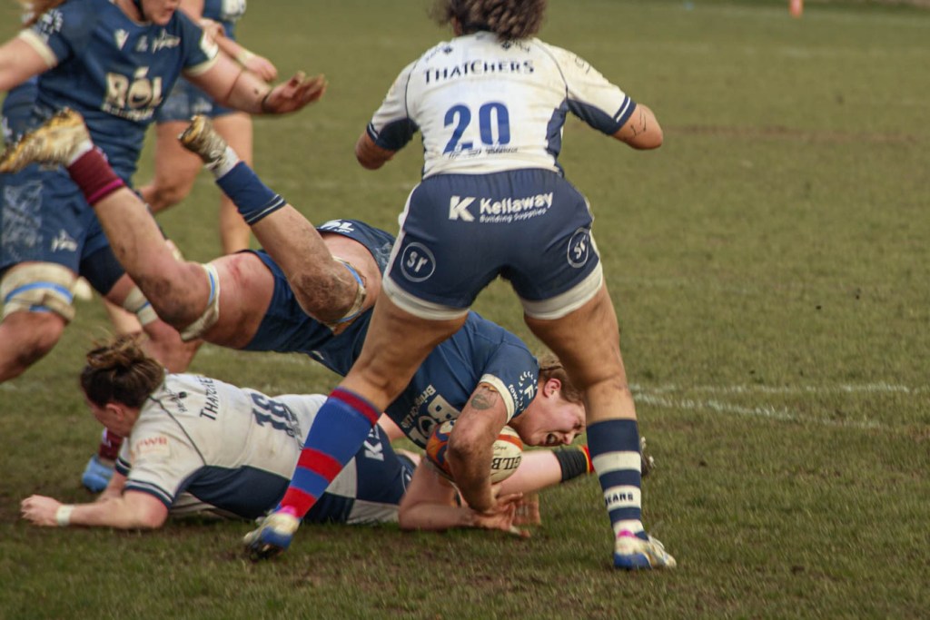 A rugby scene depicting players in action, with one player tackling another on a grassy field, showcasing athleticism and competition.